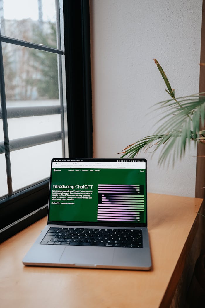 Open laptop on desk shows ChatGPT AI interface, adjacent to a large window.